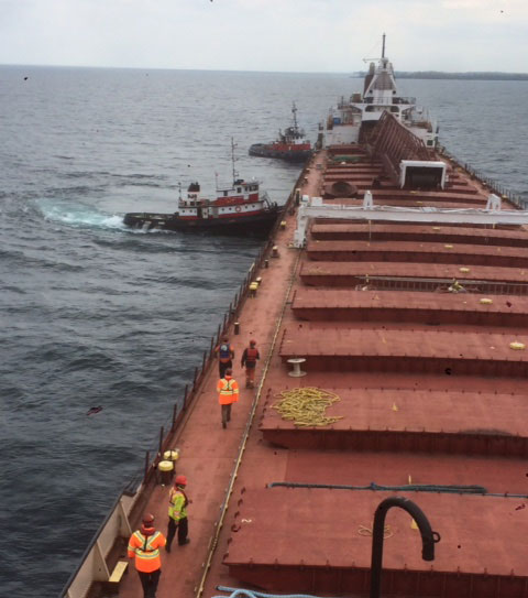 Tug boats manoeuvring the American Fortitude in Lake Ontario.